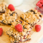 Raspberry Crumble Bars on a wooden cutting board with a glass of milk.