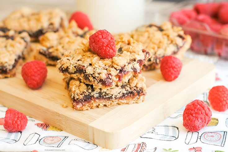 Side view of a stack of raspberry crumble bars. Fresh raspberries are scattered around the bars.