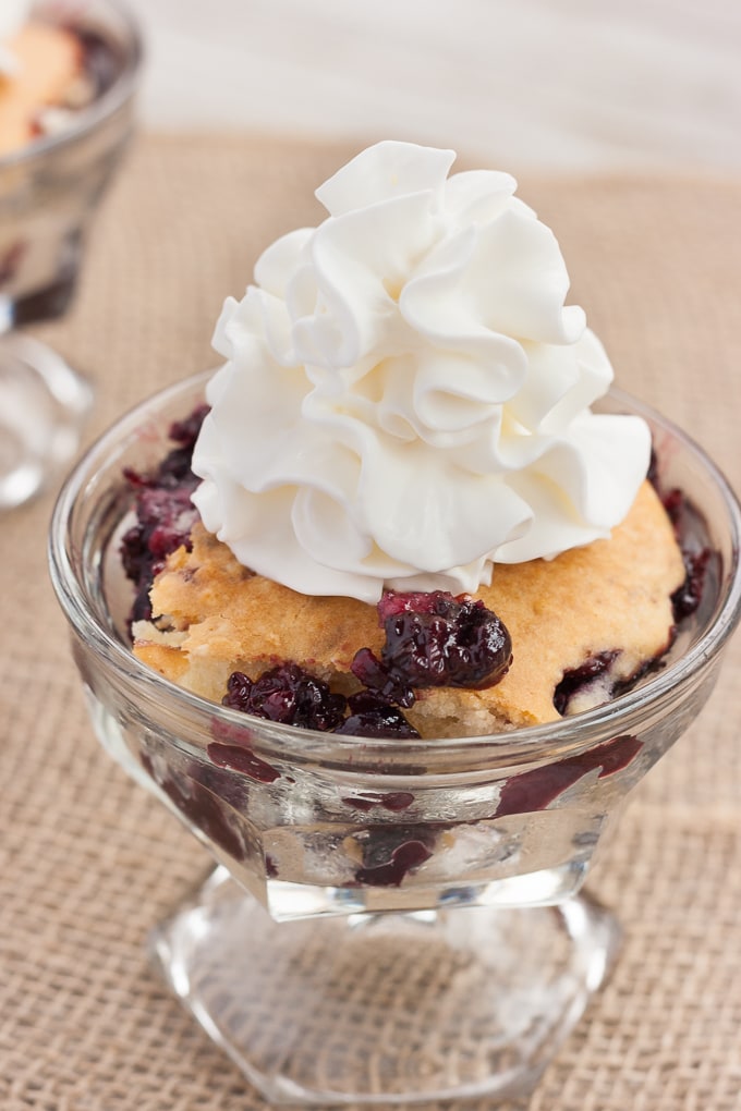 A serving of Triple Berry Cobbler in a glass dish, topped with whipped cream.