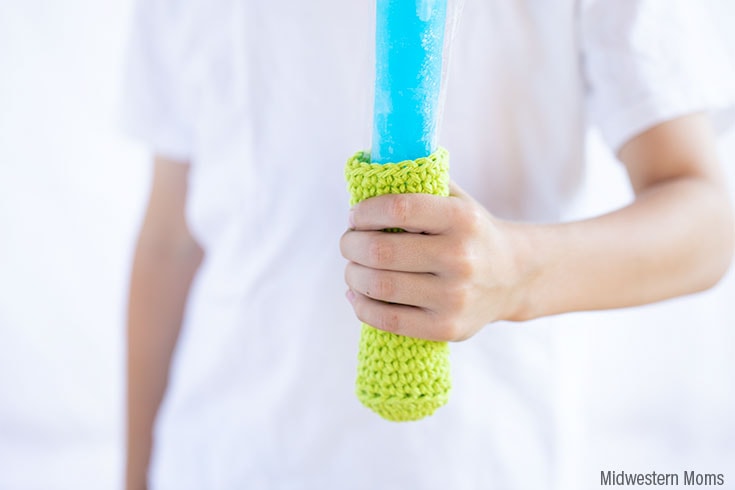Child holding a blue popsicle with a lime green crochet freezer pop holders.