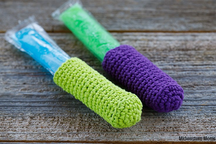 Two Popsicles laying on a wooden background. Each Freezer Pop has a crocheted freezer pop sleeve.
