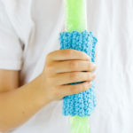 Child holding a freeze pop with a crochet sleeve to protect their hands from the cold.