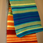 A crocheted temperature blanket draped over a blanket ladder.