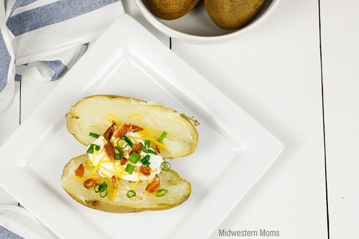 An open baked potato on a while plate. Potato is topped with bacon, cheese, sour cream, and onions. This baked potato was made in the Instant Pot.