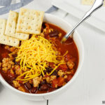 A bowl full of chili topped with shredded Cheddar cheese and saltine crackers. The chili was prepared in the instant pot.