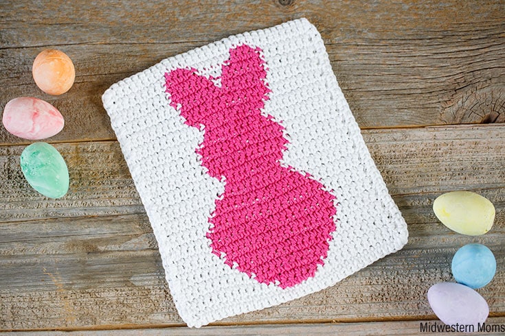 A white crochet dishcloth with a bright pink bunny on it.