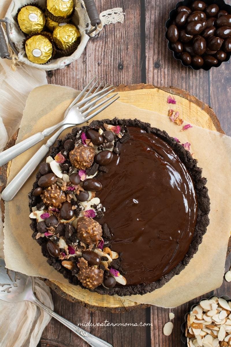 Chocolate ganache tart sitting on a wooden slab with several ingredients on the side.